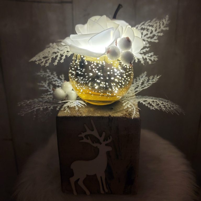 Au fil des saisons et des fêtes Vase décoratif lumineux avec fleurs blanches et feuillage sur un support en bois.