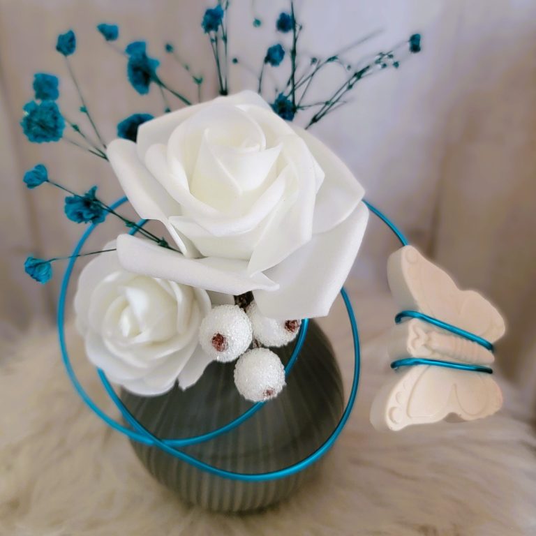 Ambiances parfumées Vase avec des roses blanches, fleurs bleues et un papillon décoratif.