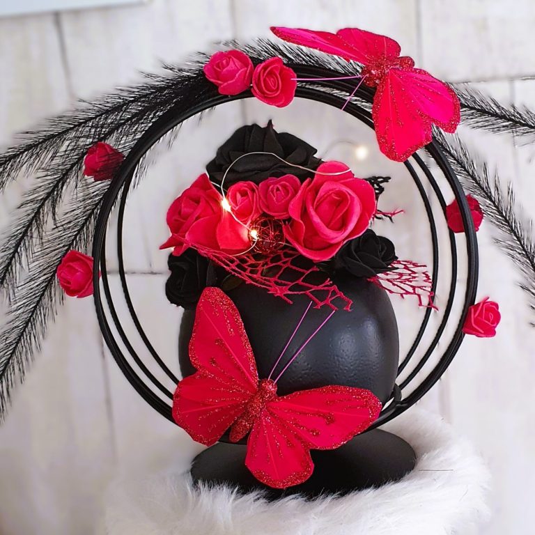 Célébrations et événements Arrangement de roses noires et rouges avec des papillons et des plumes, sur un support noir.